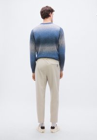 Miesten liukuvärinen pusero, jossa sinisestä harmaaseen siirtyvä väri, resorireuna hihansuissa, yhdistetty vaaleisiin beigen sävyisiin housuihin ja valkoisiin kenkiin, joissa on mustia yksityiskohtia.