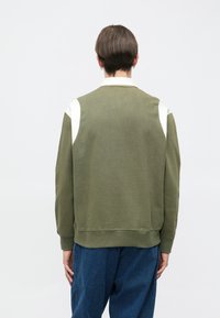 Sudadera verde oliva con acentos blancos en los hombros, puños acanalados y cuello redondo. Hecha de un material suave, con un ajuste relajado.