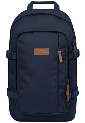 Marineblauer Rucksack mit Frontreißverschlusstasche, seitlichen Kompressionsriemen, oberem Tragegriff und braunem Markenlogo-Patch sowie Reißverschlusszügen.