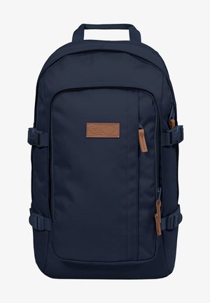 Marineblauer Rucksack mit Frontreißverschlusstasche, seitlichen Kompressionsriemen, oberem Tragegriff und braunem Markenlogo-Patch sowie Reißverschlusszügen.