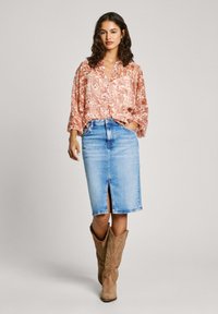 Blusa ligera de color rosa con estampado floral, cuello en V y mangas sueltas, combinada con una falda lápiz de denim azul claro hasta la rodilla con una abertura frontal.