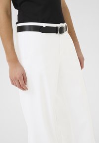 Witte wijde pantalon met een gladde textuur, voorzien van een zwarte leren riem met een zilveren gesp, gedragen met een zwart top.