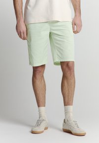 Lichtgroene katoenen shorts met een relaxte pasvorm, knielange ontwerp en een gladde textuur, gecombineerd met beige sneakers en witte sokken.