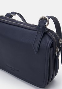 Námorníkově modrá kožená crossbody taška se zipovým uzávěrem, vybavená stříbrným kováním, dvojitými přihrádkami a texturovaným povrchem.