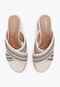 Des sandales blanches à enfiler avec des accents tissés noirs et beiges. Elles présentent une tige lisse semblable à du cuir et un design à bouts découverts.