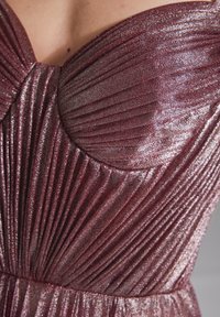 Burgundy-mekko, jossa on pleatattu pinta, sydänmuotoinen pääntie ja kimalteleva kangas, korostaen metallisia yksityiskohtia.