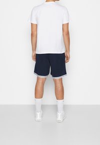 T-shirt en coton blanc et short bleu marine avec bordure blanche, assortis à des baskets blanches et des chaussettes montantes. Design épuré et simple.