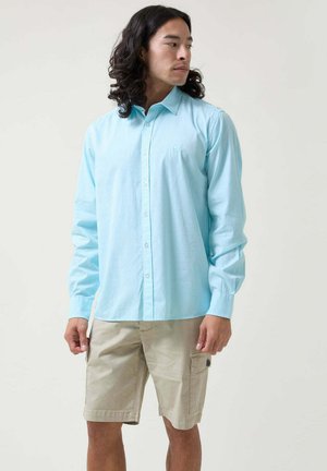 Camisa de botonada de manga larga en azul claro con cuello, combinada con pantalones cortos cargo beige que presentan bolsillos laterales y detalles cosidos.