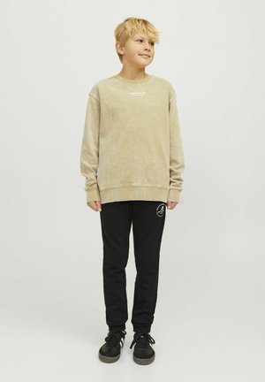 Beige, gestructureerde sweatshirt met geribde boorden en onderkant, gecombineerd met zwarte sweatpants met een logo. Zwarte sneakers maken de outfit compleet.