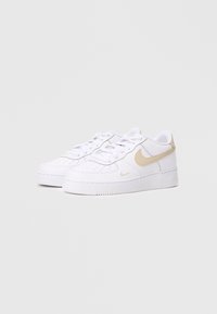 Tênis brancos em couro com textura suave, apresentando um swoosh dourado da Nike, design com atacadores e sola de borracha com padrão de ranhuras.
