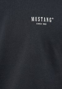 Mørkegrå T-shirt lavet af bomuld, med hvidt "MUSTANG"-logo og teksten "SINCE 1932" midt på forsiden. Glat tekstur.