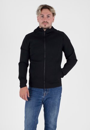Zwarte zip-up hoodie met een aansluitend ontwerp, voorzien van lange mouwen, een hoge kraag en een gestructureerde stof. G gedragen met blauwe spijkerbroeken.