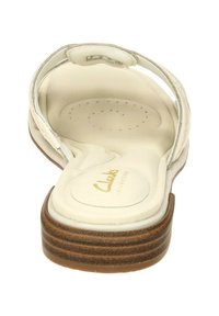 Sandal bianca con una soletta morbida, dotata di una suola arrotondata e di un accento in legno marrone. La texture sotto il piede presenta perforazioni per il comfort.