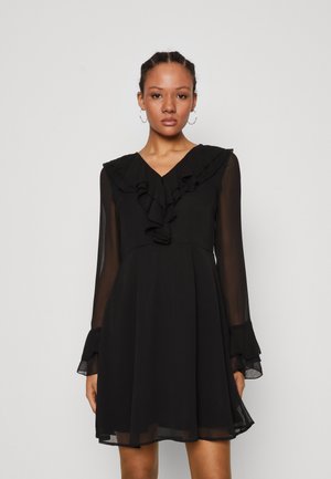 Rochie neagră din chiffon cu mâneci lungi, decolteu volanat și manșete evazate. Prezintă o talie ajustată și fustă evazată pentru o siluetă fluidă.