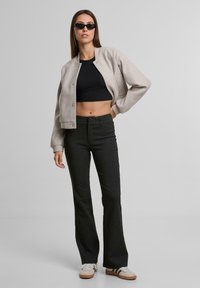 Světle šedá bomber bunda přes černý crop top, doplněná pruhovanými černými kalhotami s rozšířenými nohavicemi a bílými teniskami s černými akcenty. Černé sluneční brýle.