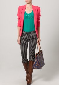 Blazer fucsia, top verde con texto de lentejuelas, pantalones rayados en blanco y negro, botas marrones hasta la rodilla, bolsa de mano azul marino con estampado.