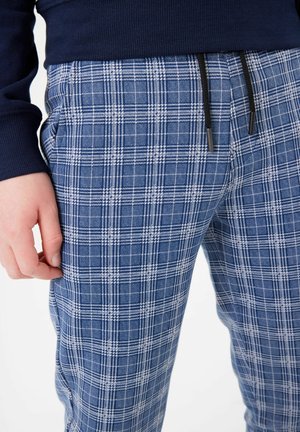 Modré a bílé kostkované pyžamové kalhoty s páskem na stažení. Obsahují boční kapsy a jsou vyrobeny z měkké, lehké látky. Volný střih.