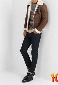 Brun läderbombarjacka med vit skinnkrage, grå stickad tröja, mörka denimjeans och svarta snörstövlar.