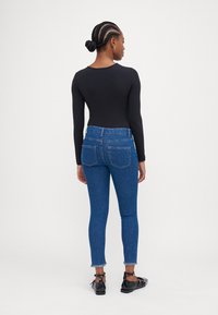 Μαύρο κορμάκι με μακριά μανίκια συνδυασμένο με μπλε κολλητά τζιν, που διαθέτουν σκισμένο στρίφωμα και πίσω τσέπες. Το μοντέλο φοράει μαύρα παπούτσια με κορδόνια.