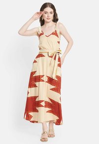 Robe maxi en crème avec des motifs en zigzag rouge vif et à pois, dotée de volants aux épaules et d'une ceinture nouée à la taille. Sandales plates dorées incluses.
