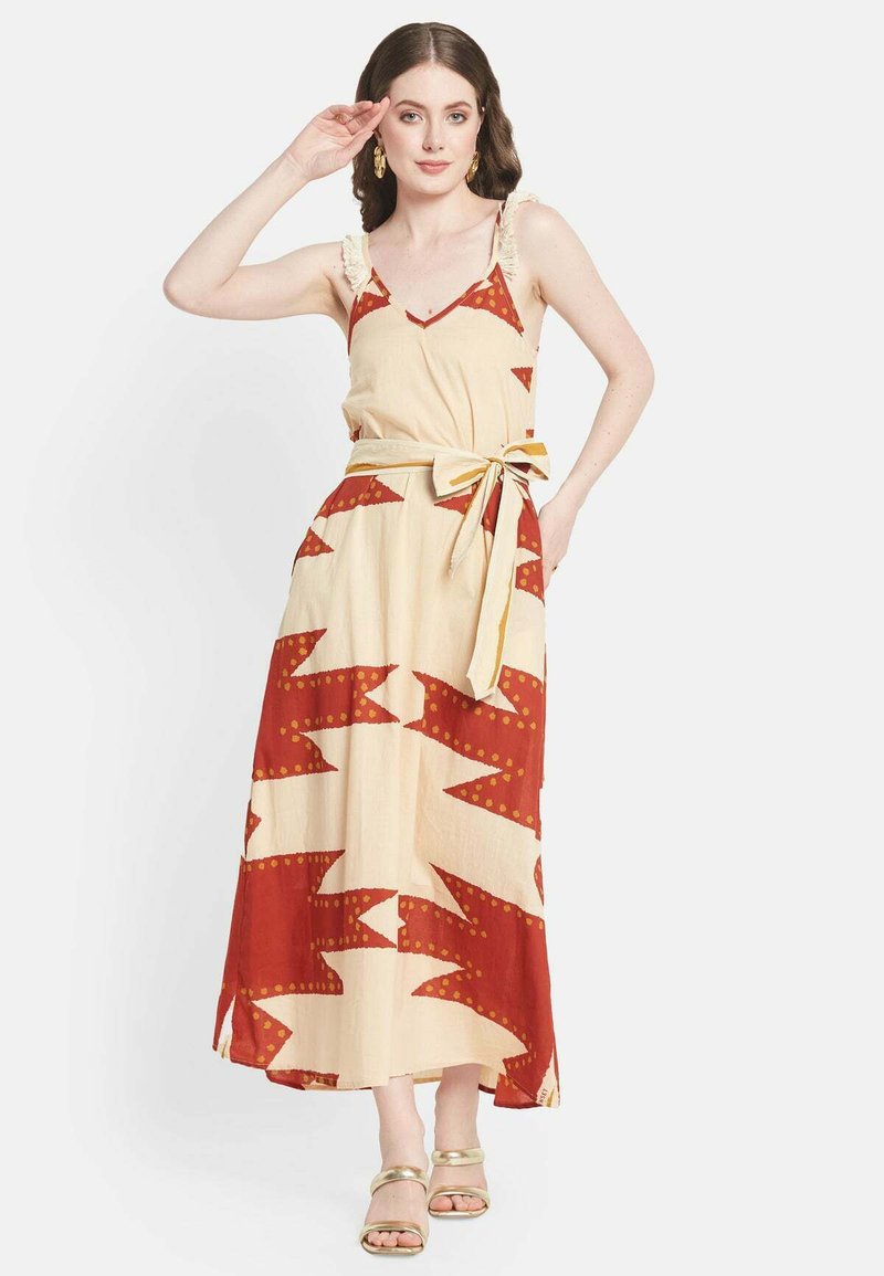 Robe maxi en crème avec des motifs en zigzag rouge vif et à pois, dotée de volants aux épaules et d'une ceinture nouée à la taille. Sandales plates dorées incluses.