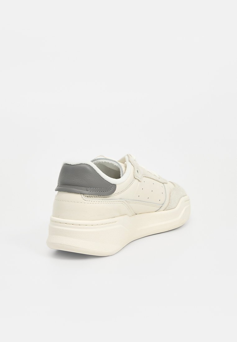 Baskets blanches avec une section en daim texturé, des accents en cuir gris, un col rembourré et des perforations sur les côtés.
