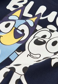 Marineblå T-skjorte med en tegneserieillustrasjon av to dyrefigurer, en i lyseblå og den andre i hvit med svarte flekker.