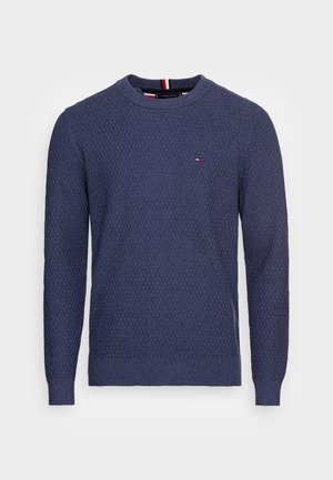 Pull en maille bleu marine à manches longues avec col rond, petit logo rouge, blanc et bleu sur la poitrine gauche, poignets et ourlet côtelés.