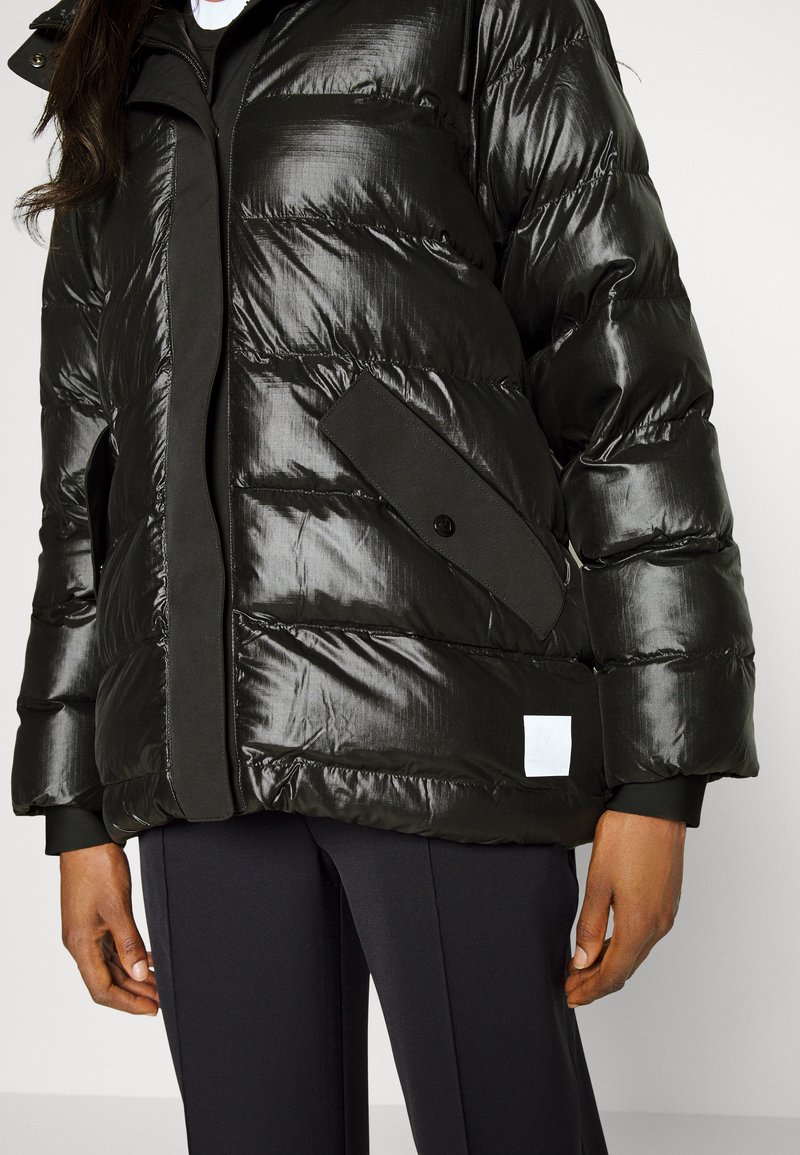Schwarze Pufferjacke mit glänzender, strukturiertem Finish. Verfügt über eine Frontklapptasche, Druckknopf und einen kontrastierenden Stoffbesatz.