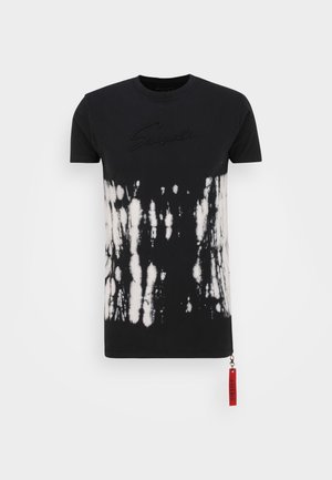 Schwarzes T-Shirt mit kurzen Ärmeln und weißem Batikmuster auf der unteren Hälfte, erhabener schwarzer Schriftzug auf der Brust und einem roten Stoffetikett am Saum.