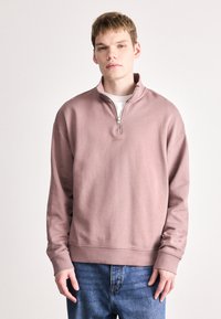 Mikina s krátkým zipem v jemně růžovém provedení, uvolněný střih, žebrované manžety a lem, s jemným vyšitým logem na přední straně.