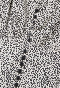 Tkanina we wzór lamparta z czarnymi guzikami po boku. Teksturowana powierzchnia na kremowym tle z wyraźnymi czarnymi plamami.