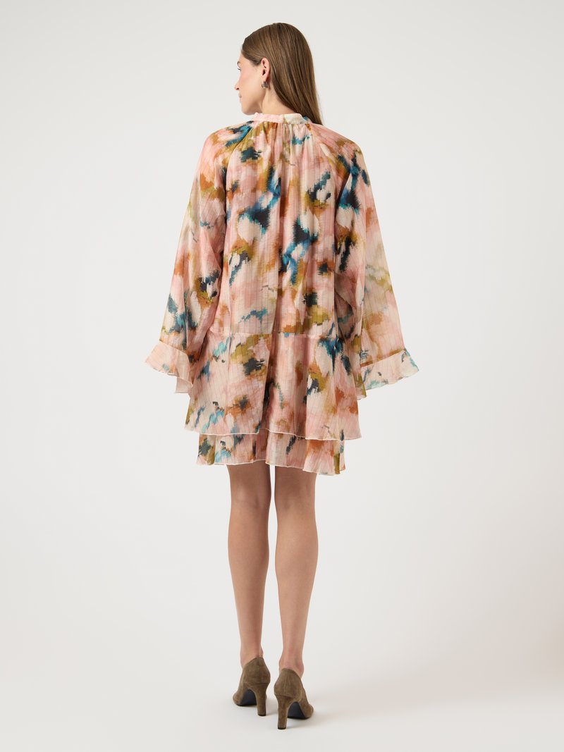 Γυναίκα με μακριά μαλλιά που φοράει ένα αέρινο, στρωματοποιημένο φόρεμα με λουλουδάτο μοτίβο σε ροζ, μπλε και καφέ αποχρώσεις, συνδυασμένο με καφέ σουέντ τακούνια.