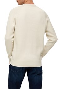 Licht crèmekleurige geribde trui met een ronde halslijn, voorzien van lange mouwen en een rechte zoom. Gecombineerd met donkerblauwe jeans.