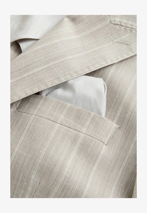Giacca da completo beige a righe sottili con un fazzoletto da taschino grigio chiaro piegato ordinatamente nella tasca a petto.