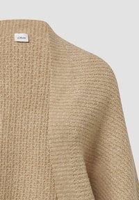 Beżowy sweter z dzianiny, charakteryzujący się teksturą prążkowaną i otwartym przodem. Metka przyszyta w pobliżu dekoltu. Miękki, ciepły materiał.