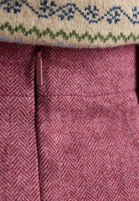 Wełniany sweter z dzianiny w kremowej bazie z niebiesko-zielonym wzorem, nałożony na różową tkaninę o wzorze jodełki z zamkiem błyskawicznym.