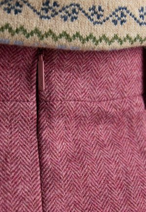 Vlněný pletený svetr s krémovým základem a modrozelenými vzory, vrstvený přes růžovou tkaninu se vzorem rybí kosti a zipem.