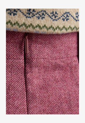 Vlnený pletený sveter s krémovým základom a modrozelenými vzormi, vrstvený cez ružovú tkaninu so vzorom rybej kosti s uzáverom na zips.