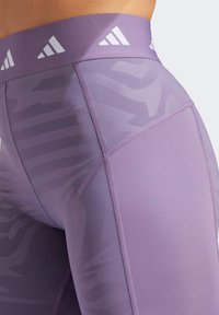 Fioletowe legginsy sportowe z fakturowanym wzorem i subtelnym motywem, elastycznym pasem w talii z białymi akcentami logo oraz przeszyciami.