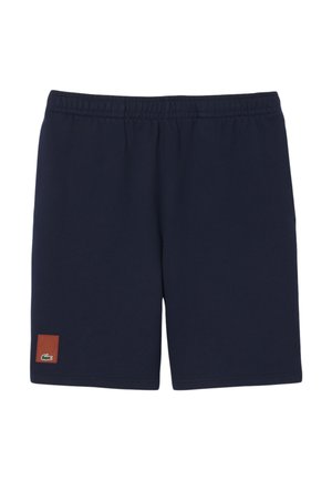 Pantalones cortos con cintura elástica azul marino con un pequeño parche marrón y un logo de cocodrilo verde cerca del borde inferior de la pierna izquierda.