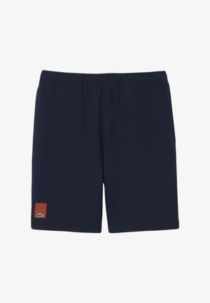 Pantalones cortos con cintura elástica azul marino con un pequeño parche marrón y un logo de cocodrilo verde cerca del borde inferior de la pierna izquierda.