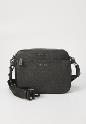 Sacoche en textile noir avec motif en relief du logo, quincaillerie en ton argent, poche zippée et bandoulière réglable. Forme rectangulaire.