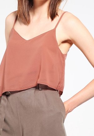 Blouse sans manches rose, avec un col en V, fabriquée en tissu léger. Elle présente une coupe ample et un ourlet légèrement courbé.