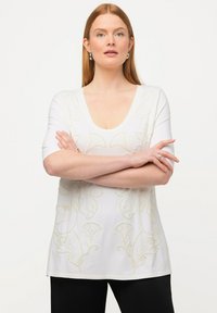 Top blanco de manga corta con tejido suave, que presenta intrincados bordados florales en beige, un escote amplio y un corte relajado.