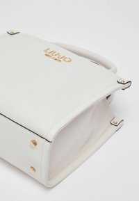 Sac à main en cuir blanc avec des accents en métal doré et une surface texturée. Présente une forme structurée et un logo embossé à l'avant.