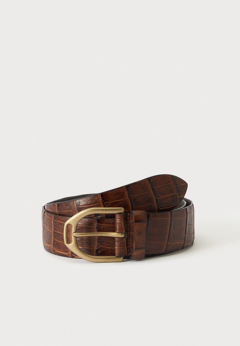 Ceinture en cuir marron à texture crocodile avec boucle en laiton enroulée sur un fond blanc.