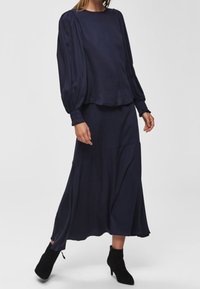 Mörkblå ensemble med en lös, långärmad topp med rynkade axlar och en flödande, medellång kjol. Tillsammans med svarta ankelskor.