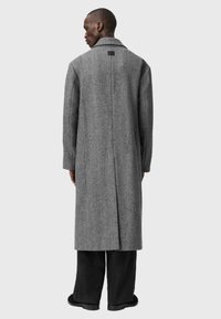 Pelēks vilnas maisījuma virsjakas ar šķautņu rakstu, ar vienu šķērsu venti, un plašiem uzmavu galiem. Valkāts virs melniem biksēm, minimāla zīmola identifikācija uz apkakles.