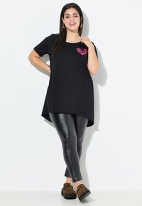 Zwarte tuniek met een ronde halslijn en een roze panda-afbeelding. Gecombineerd met glanzende zwarte leggings en bruine platform schoenen met een luipaardprint.